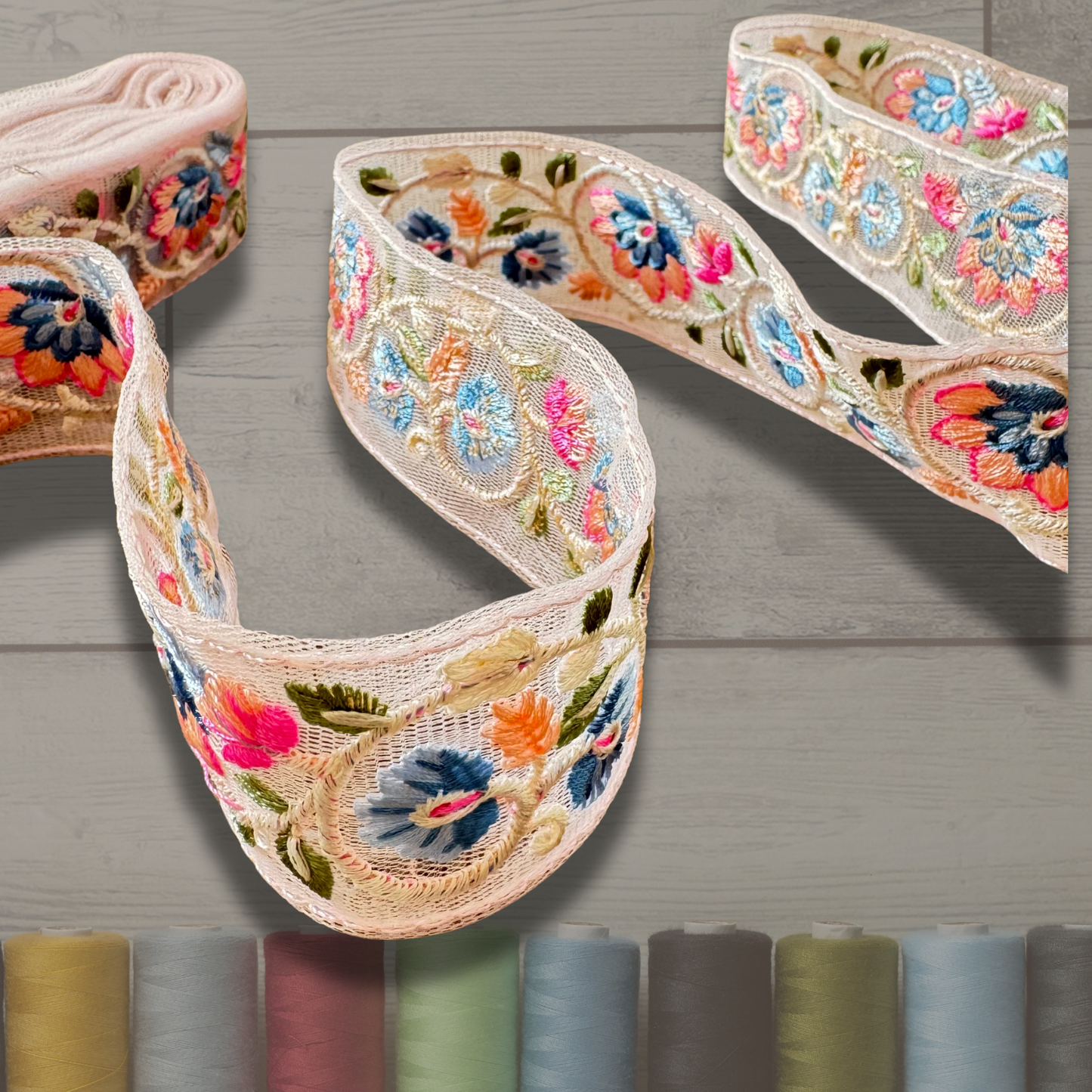 Tresa Embroidered Trim close up on an asthetic background with thread spools on the bottom