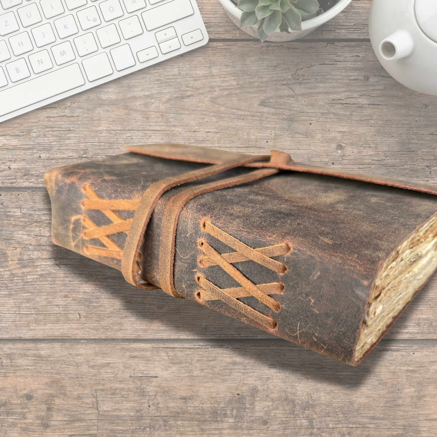 leather journal for men on an asthetic wooden table with keyboard and a tea kettle with a small flower pot on the side