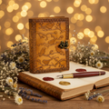 Decorative leather-bound book with floral design, pen, and wax seals on a wooden surface with blurred lights in the background.
