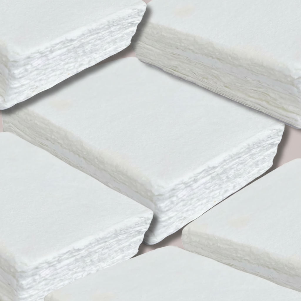 Macro close up of stacked white handmade cotton deckle edge paper sheets showing soft velvety surface texture and rough natural torn edges