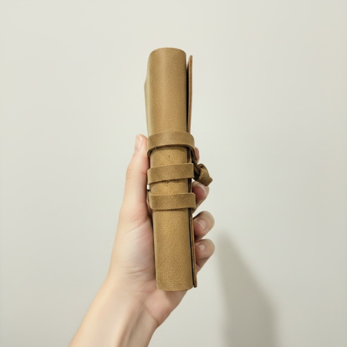 Hand holding a rolled handmade leather bound journal showing wrap strap and thickness – premium leather journal Australia, unique gift for her or graduation gift