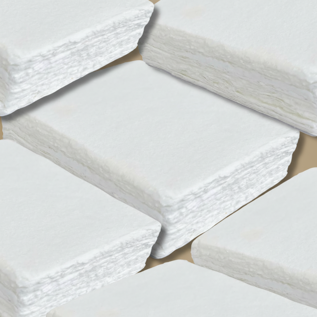 Close-up of multiple stacks of white 250 GSM handmade cotton rag paper showing rough natural deckle edges and cotton fibre texture, ideal for wedding invitations and calligraphy