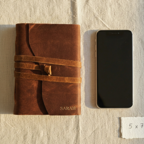 Personalised leather journal with wrap bands and embossed gold name Sarah kept beside smartphone — graduation gift for her, leather journal Australia
