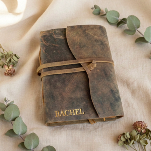 Personalised leather journal Australia with gold embossed name RACHEL, flat lay with eucalyptus and dried flowers on linen — handmade leather journal gift for her