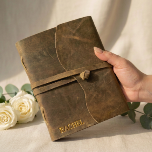 Handmade leather journal with gold embossed name RACHEL held in hand, white roses and eucalyptus background — personalised leather journal gift for her Australia
