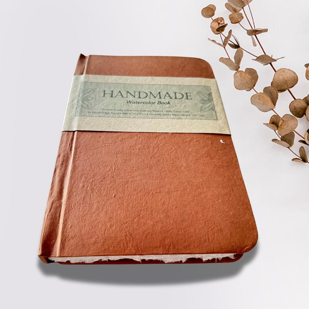 Watercolour sketchbook on a white plain background with dried leaves on the side.