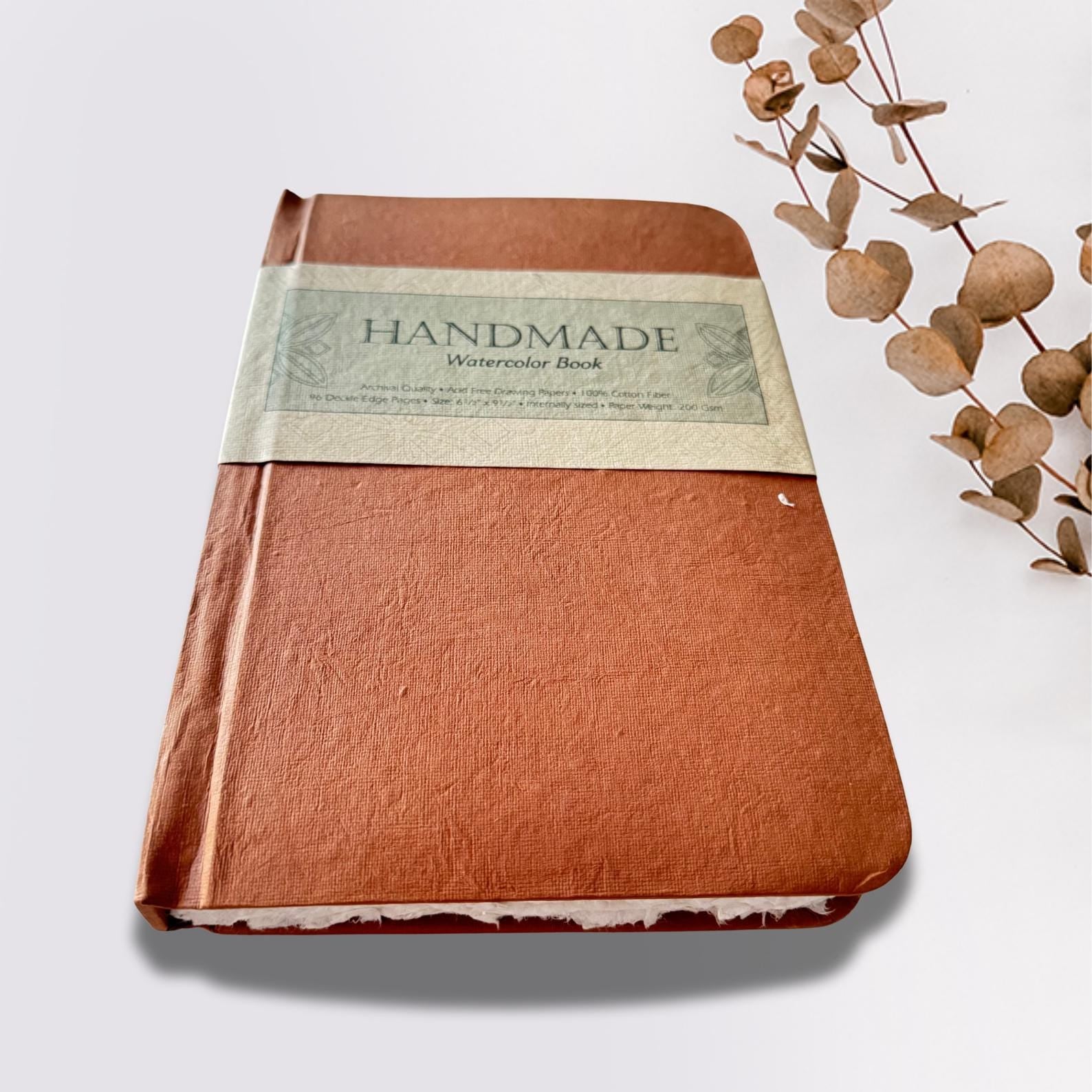 Watercolour sketchbook on a white plain background with dried leaves on the side.